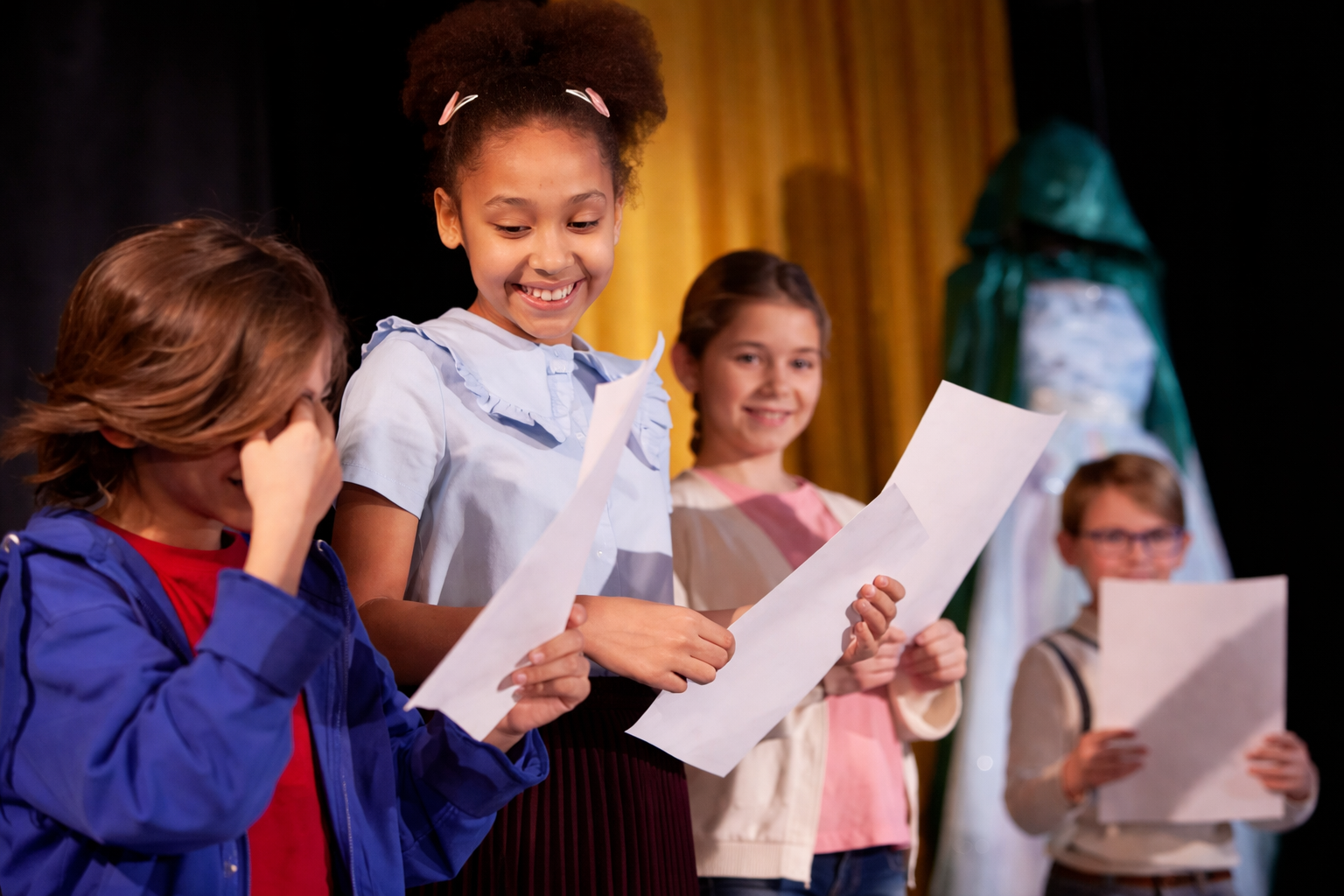Young students on stage holding scripts during a musical theater rehearsal.