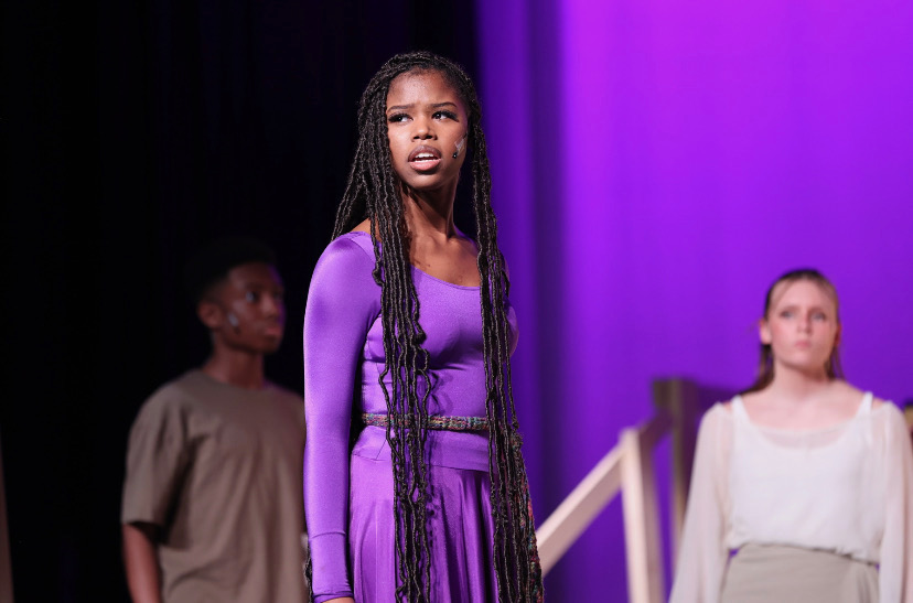 Jordan Griffin performing on stage in a purple costume during a musical theater showcase